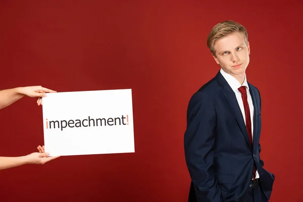 Skeptical man grimacing near white card with impeachment lettering on red background — Stock Photo