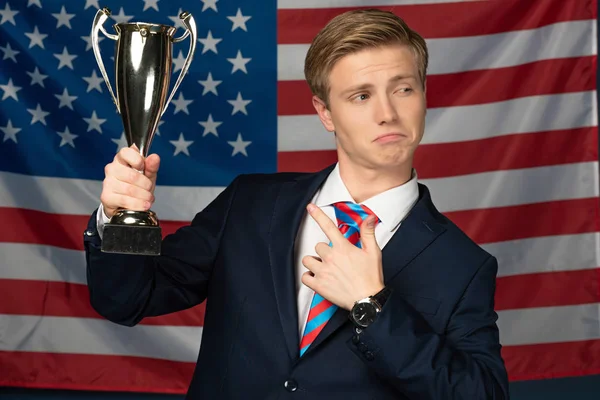 Hombre señalando con el dedo a copa dorada sobre fondo de bandera americana — Stock Photo