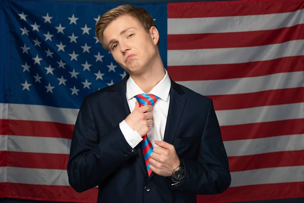 Hombre serio tocando corbata en fondo de bandera americana - foto de stock