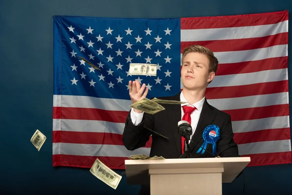 Hombre lanzando dinero en efectivo en tribuna en fondo de bandera americana — Stock Photo