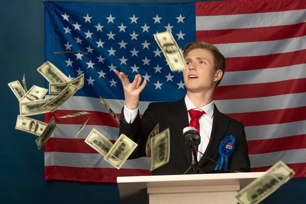 Hombre lanzando dinero en efectivo en tribuna en fondo de bandera americana - foto de stock