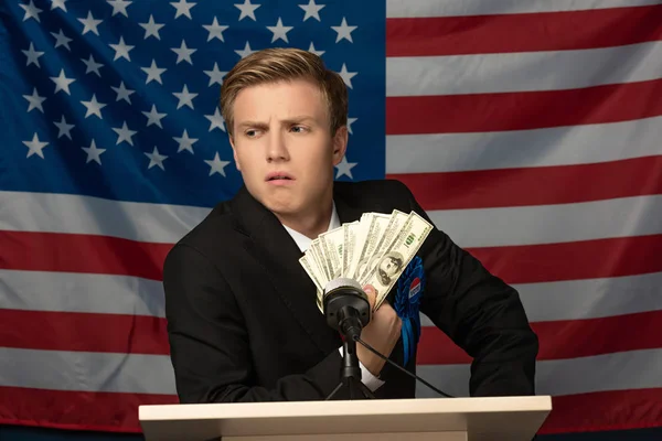 Hombre sosteniendo efectivo en tribuna en fondo de bandera americana - foto de stock
