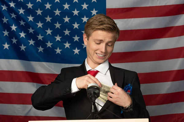 Hombre sosteniendo efectivo en tribuna en fondo de bandera americana — Stock Photo