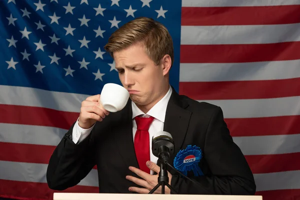 Homem olhando para xícara de café no tribuno no fundo bandeira americana — Fotografia de Stock