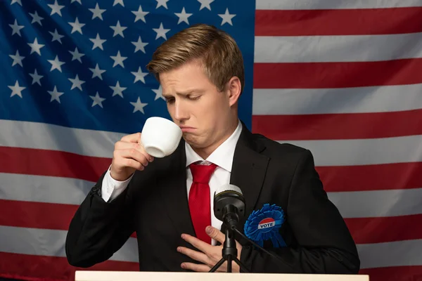 Mann blickt auf Kaffeetasse auf Tribüne auf Hintergrund amerikanischer Flagge — Stockfoto