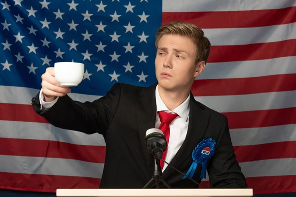 Hombre mirando taza de café en tribuna en fondo de bandera americana — Stock Photo