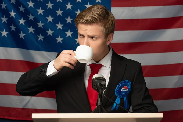 Homem bebendo café no tribuno no fundo bandeira americana — Fotografia de Stock