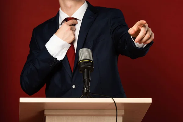 Vista recortada del hombre señalando con el dedo en tribuna sobre fondo rojo — Stock Photo