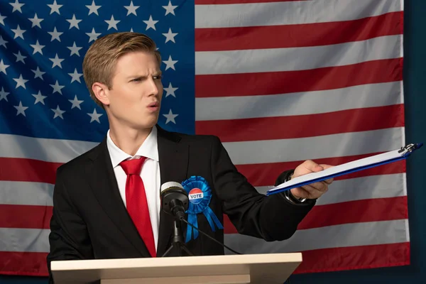 Emotional man holing clipboard on tribune on american flag background — Stock Photo