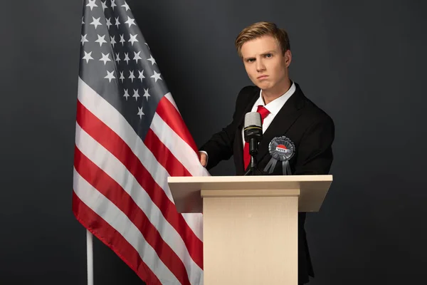 Hombre serio en tribuna con bandera americana sobre fondo negro - foto de stock