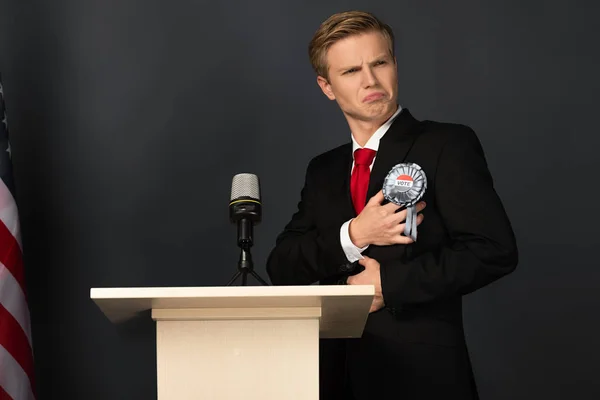 Emotionaler Mann berührt Abzeichen auf Tribüne auf schwarzem Hintergrund — Stockfoto