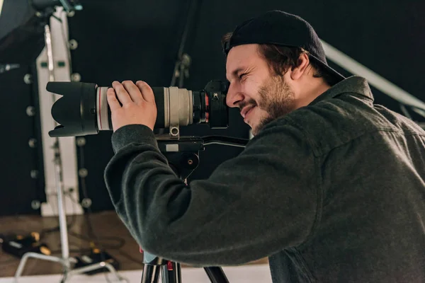 Side view of smiling cameraman with camera at workplace — Stock Photo