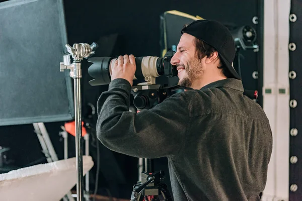 Seitenansicht eines lächelnden Videofilmers mit Kamera im Fotostudio — Stockfoto