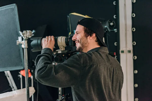 Vista laterale del bellissimo cameraman sorridente che lavora in studio fotografico — Foto stock