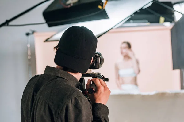 Vista trasera del camarógrafo trabajando con modelo femenino en estudio fotográfico - foto de stock