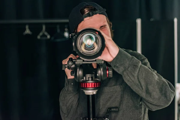 Videógrafo mirando a través de la cámara en el estudio de fotografía - foto de stock