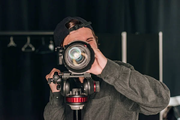 Videógrafo mirando a través de la cámara mientras trabaja en un estudio de fotografía - foto de stock