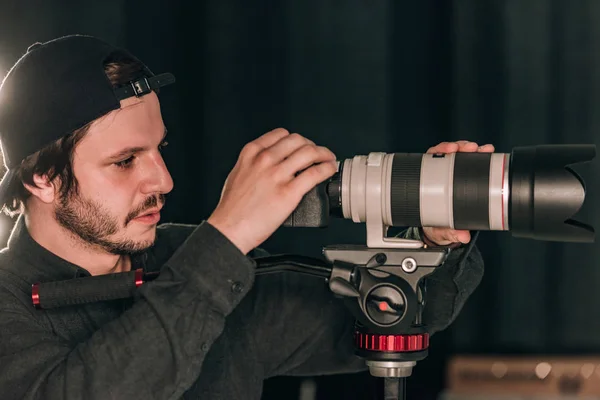 Vista lateral do videógrafo olhando para a exibição da câmera enquanto trabalhava no estúdio de fotografia — Fotografia de Stock