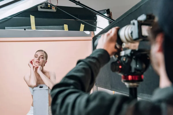 Selective focus of attractive model posing to videographer with camera in photo studio — Stock Photo