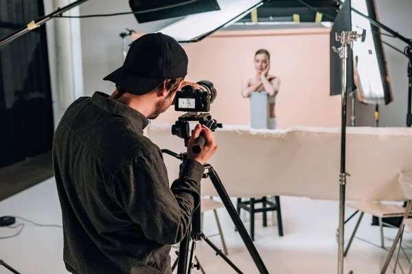 Foco seletivo do cinegrafista filmando modelo bonito no estúdio de fotos com holofotes — Fotografia de Stock