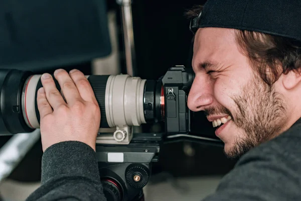 Vista lateral de un guapo camarógrafo sonriente con cámara - foto de stock