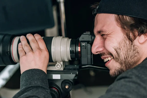 Vue latérale du beau vidéaste souriant avec caméra — Photo de stock