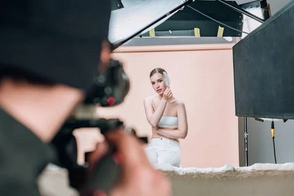 Selective focus of beautiful model with feather posing to videographer in photo studio — Stock Photo