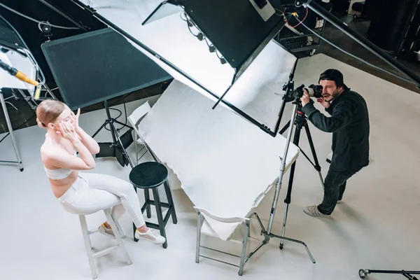 Visão aérea de belo modelo e videógrafo trabalhando em estúdio de fotografia com holofotes — Fotografia de Stock