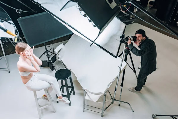 Vista aérea de la hermosa modelo y videógrafo que trabaja en el estudio de fotografía con proyectores - foto de stock