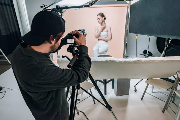 Cameraman olhando para a exibição da câmera enquanto filma modelo atraente no estúdio de fotos — Fotografia de Stock