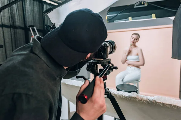 Visão traseira do videógrafo filmando modelo atraente com rolo de massagem sob holofotes — Fotografia de Stock