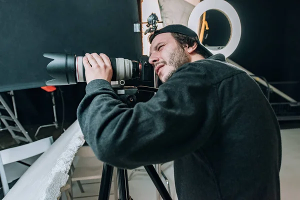 Vista lateral del videógrafo con cámara en trípode en estudio fotográfico - foto de stock