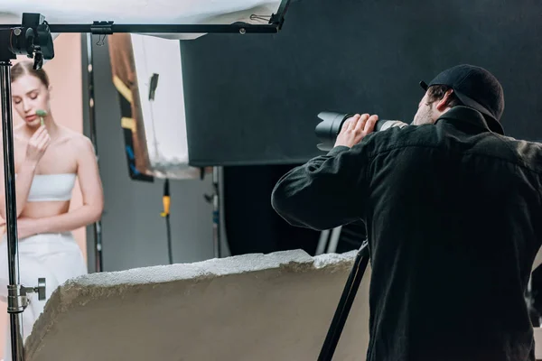 Selective focus of cameraman and attractive model with massage roller in photo studio with spotlights — Stock Photo