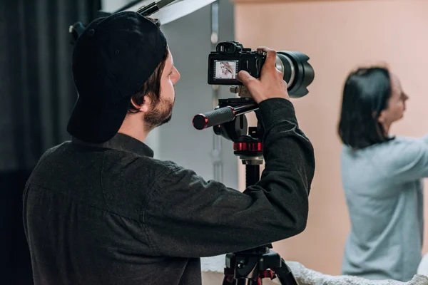 Mise au point sélective du vidéaste avec assistant et modèle travaillant en studio photo — Photo de stock