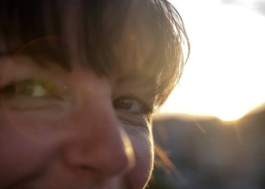 Gün batımında gülümseyen esmer bir kadının mutlu bakışları.