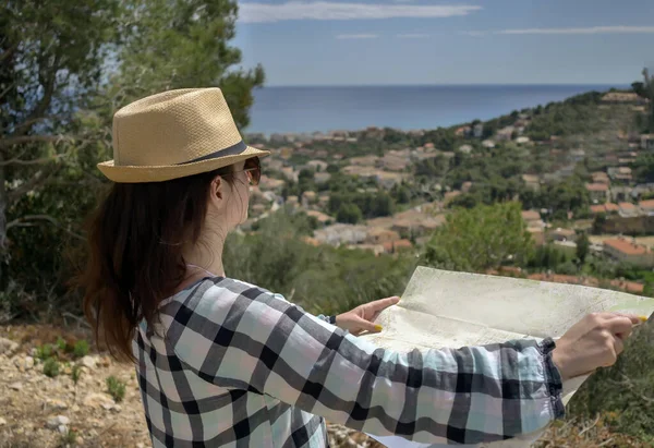 Brunette fille dans un chapeau se tient sur une montagne tient une carte de la région dans ses mains, copyspace — Photo