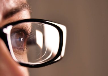 Gri arka planda siyah çerçeveli gözlüklü bir kızın açık kahverengi gözleri.