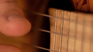 Erkek parmaklar klasik bir gitarın tellerinde çalıyor, yakın plan.