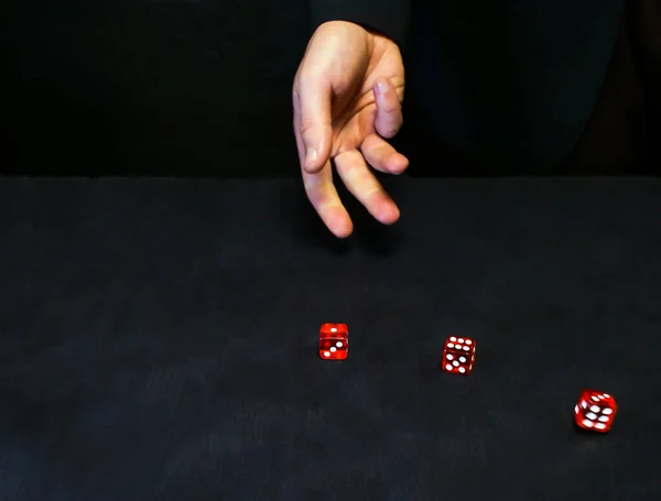 Man throws red dice on a black table surface, casino concept