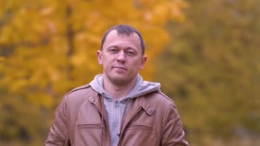 Sonbahar parkında kameraya bakıp gülümseyen genç bir adamın portresi.