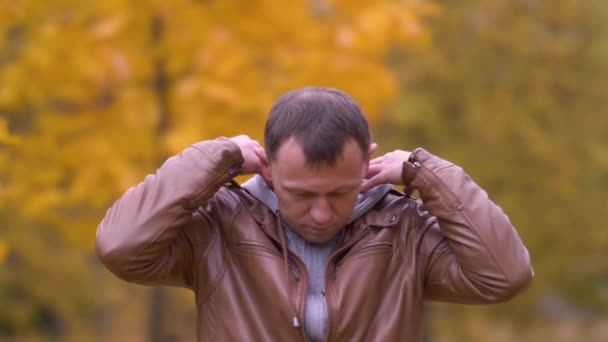 Attractive young man stands in a park and puts on a hood — Stock Video