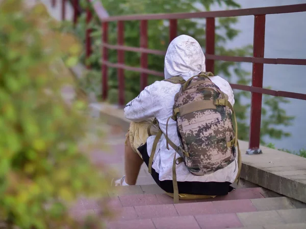 Un homme seul avec un sac à dos s'assoit les mains serrées sur les marches des escaliers en béton dans le parc — Photo