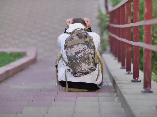 Un homme seul avec un sac à dos s'assoit les mains serrées sur les marches des escaliers en béton — Photo