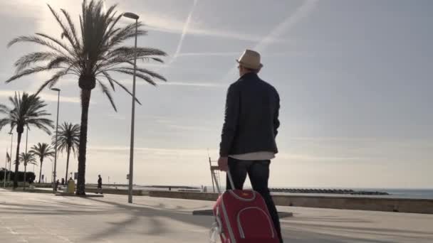 Viajero Con Sombrero Una Maleta Roja Pasea Por Paseo Marítimo — Vídeo de stock