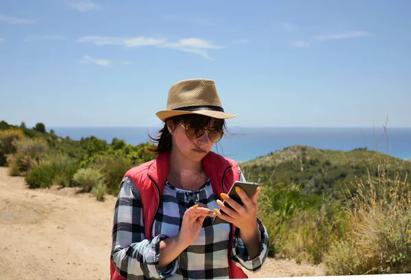 Lány turista néz egy mobiltelefon, miközben kint áll egy napsütéses napon Stock Fotó