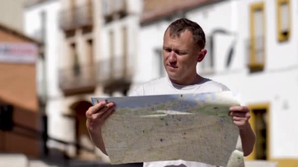 Ταξιδιώτης κρατά στα χέρια του ένα χάρτη της πόλης, στέκεται στο δρόμο και εξετάζει ένα χάρτη — Αρχείο Βίντεο