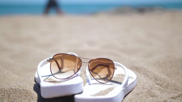 Zapatillas blancas con gafas de sol en la arena de una playa, atleta corriendo contra el telón de fondo — Vídeo de stock