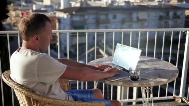 Jovem freelancer masculino está trabalhando em um laptop enquanto está sentado em uma varanda — Vídeo de Stock