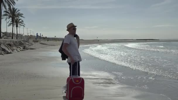 Viaggiatore uomo con una valigia rossa è venuto al mare in vacanza, emozioni positive — Video Stock