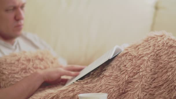 Attraktiver Mann blickt auf ein Buch, das zu Hause auf der Couch liegt — Stockvideo